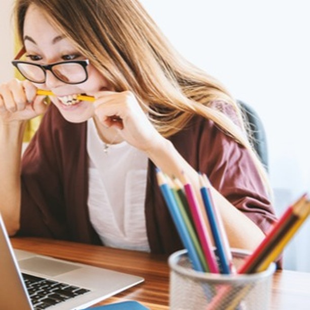 girl with laptop press pen inside her teeth